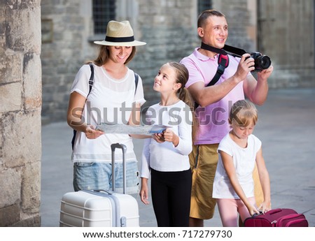 Portrait of young parents tourists with children using map and making photo on vacation
