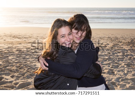Mature mother with her teenage daughter looking in one direction on beach backlit with sun