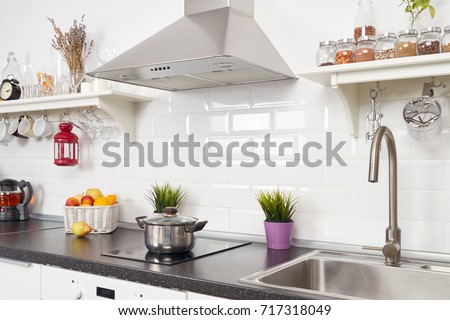 Blurred interior of a light kitchen in the apartment. Bright home interior decoration items, fruit, flowers in a pot, steel hood. Bright ready-made picture for your individual design