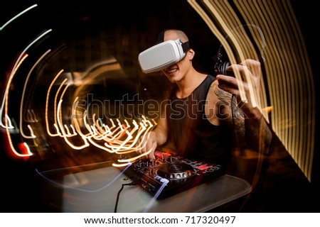 Sporty young guy DJ in glasses of virtual reality against the background of a night city. The concept of the future Royalty-Free Stock Photo #717320497