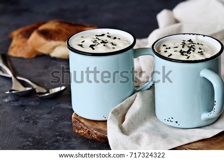 Hot potato soup with dried chives served in enamel cups with sliced, toasted bread. Extreme shallow depth of field with selective focus on cup in foreground.