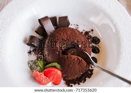 Tasting of chocolate fondant in restaurant. Delicious creamy dessert with decoration from strawberry and mint, close up picture