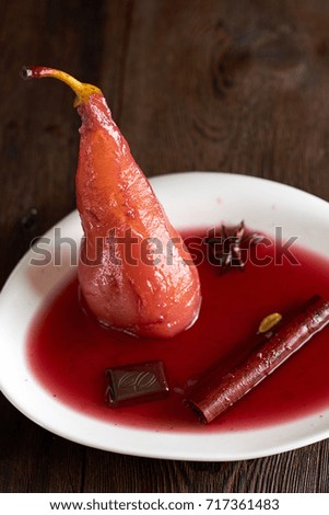 pear in red wine on a white plate with cinnamon and star anise on the table dark wood