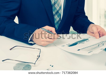 business documents on office table with laptop computer and graph financial digital diagram and businessman working in the background