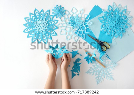 Making of snowflakes from blue paper. The child's hands on a white background hold a snowflake