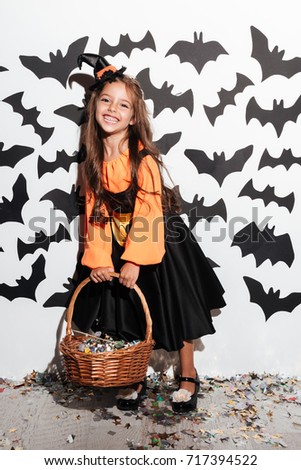 Cheerful little girl dressed in halloween costume posing and laughing with bats on a background