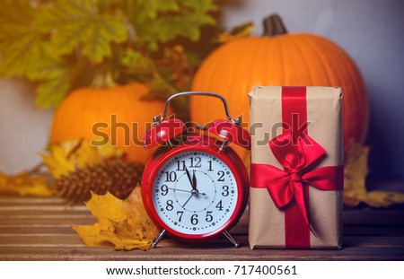 Retro alarm clock with leaves and pumpkin with Halloween gift box on background. Autumn season image composition