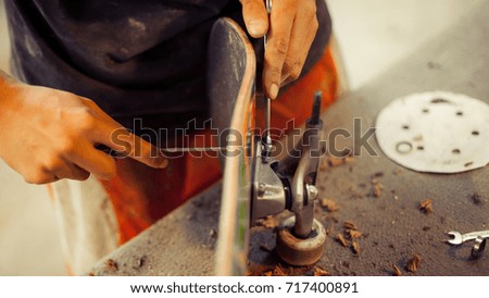 Young man in carpentry workshop fixing wheel on his skateboard. Close up