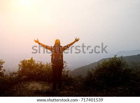 Asian hiker man with backpack standing raised hands on top of a mountain,enjoying nature view.