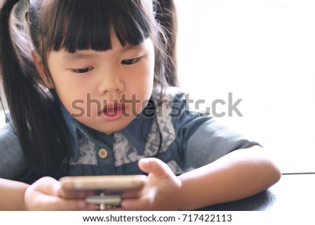 Asian children cute or kid girl wearing jeans with looking smartphone screen for vdo clip or cartoon and playing the game very concentrate which causes ADHD or Hyperactive on white background