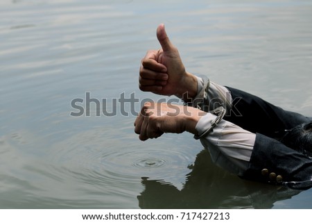 Businessman handcuffed drowning man holds his thumbs up above the water.