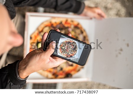 Social media influencer millennial hipster makes photo of his fresh hot out of the box delivery take away pizza on his smartphone for sharing online with followers