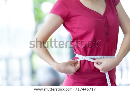Sport woman measuring her waist by using waistline or tape, comparing her waist size before and after workout for firming body, diet with accessory equipment in gym- Healthcare concept Royalty-Free Stock Photo #717445717