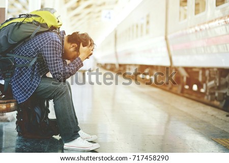 the tourist backpack man arrived late at the station. depressed and strain traveler sad sitting waiting at train station after mistakes a train makes wasting time in traveling. Royalty-Free Stock Photo #717458290