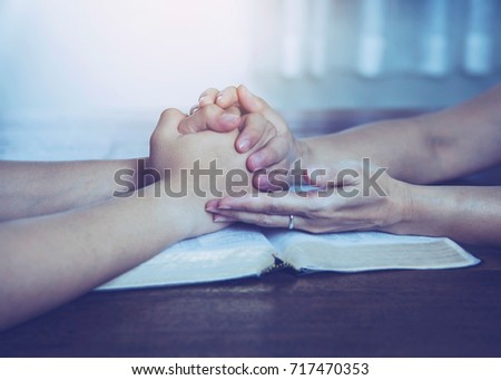 Two  people are praying together over holy bible on wooden table 