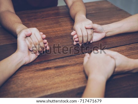 Three people are holding hands and pray together on wooden table 
