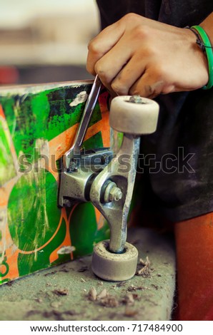 Young man in carpentry workshop fixing wheel on his skateboard. Close up