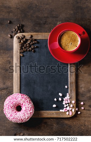 Empty vintage chalkboard, pink glazed donut, sugar, coffee beans and red cup of black coffee over old wooden background. Top view with space for text.