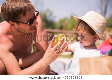 Portrait of young father who giving corn to little cute son outdoors