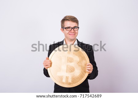 Happy cheerful young businessman holding big golden bitcoin on white background. Crypto currency, virtual money, internet and economics concept