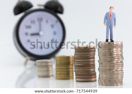 Miniature  businessman and money coin stack with blur watches background.
Small figure standing on stack of coin growing for finance blured alarm clock background.
Growing money and financial concept.