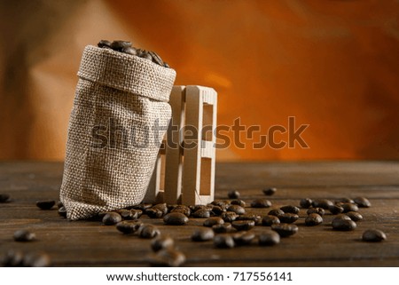 Coffee beans in a small bag on a wooden table at orange background. Empty copy space.