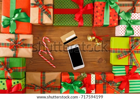 Lots of Gift boxes, xmas bells, xmas candy on wood background top view, flat lay. Presents in craft and colored paper decorated with red and green ribbon bows. Mobile phone, card.