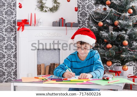Writing letter to santa. Cute boy in santa hat makes wish list of presents for christmas. Waiting for gift. Prepare for winter holidays. Child portrait, vertical image