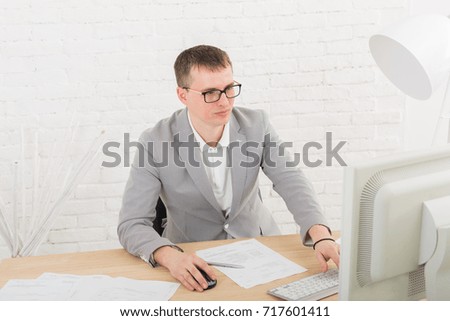 Young businessman working with laptop in modern white office interior. Handsome man in suit, successful employee at work with computer. Lifestyle portrait