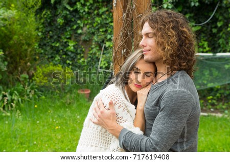 Happy couple in love at outdoors, leaning on her boyfriend's chest in a patio backyard background