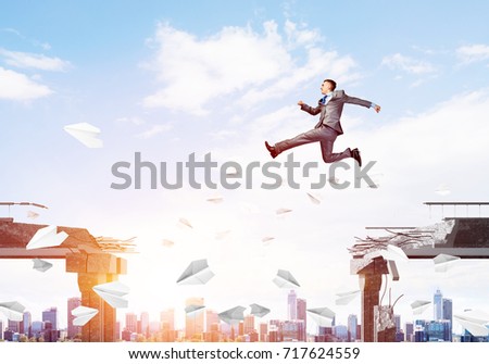 Businessman jumping over gap with flying paper planes in concrete bridge as symbol of overcoming challenges. Cityscape with sunlight on background. 3D rendering.