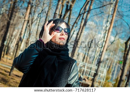 Bright beautiful picture where a young woman brunette in sunglasses looks up at the sky in the park in spring or autumn