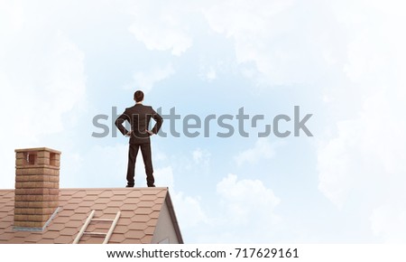 Young determined businessman standing with back on house roof and looking away. Mixed media