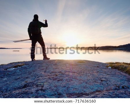 Tourist guy taking pictures of amazing sea landscape on mobile phone digital camera. Hiker stay on a rock near the smooth ocean. A beautiful sunset light create background with copy space.