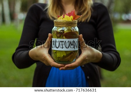 A beautiful image of a girl with a glass jar with autumn leaves and the inscription "Autumn" in her hands. Face is not visible.
