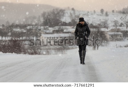 Woman in winter clothes walking on a road surrounded by snow and falling snow. Wintertime concept.