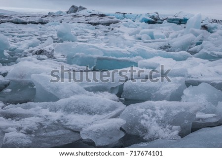 Glaciers float on the still water with underneath rocks. The ice mountain is on background. Jokulsarlon, Iceland, wintertime.