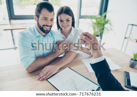 Welcome to new life! Happy young couple is embracing, getting a key from their future apartment from a broker, they signed contract, dressed in formal outfits