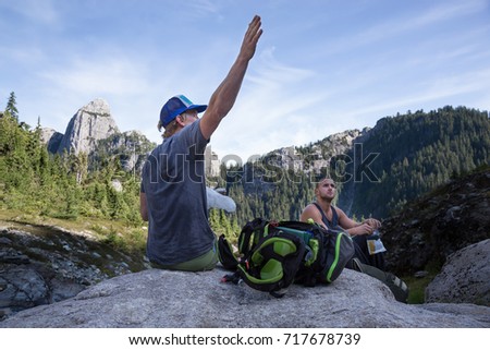 Couple of adventurous young friends are sitting and relaxing on the rock and looking at their hiking destination. Picture taken on the ascent to Skypilot Mountain near Squamish, BC, Canada.