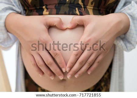 Young pregnant woman holds her hands on her swollen belly. Love concept. Horizontal with copy space. She makes heart finger on her stomach. Wearing solider bikini. 