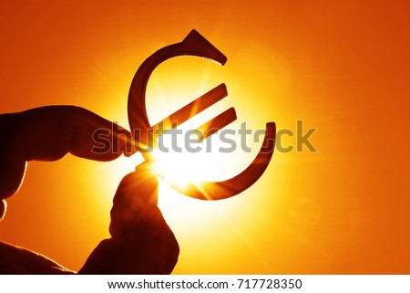 man's hand hold the Euro icon silhouette against sunny golden, yellow sky. sun rays. euro sign, symbol of money, idea of Euro Union