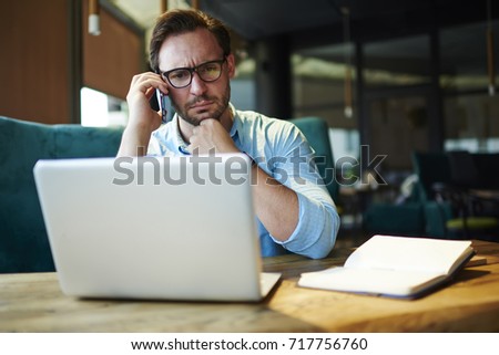 Pensive businessman in trendy spectacles having serious phone conversation with colleague while solving problem with report online.Thoughtful boss concentrated on checking accountings on laptop
 Royalty-Free Stock Photo #717756760