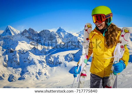 Skier teenager along a snowy ridge with skis. In background blue sky and shiny sun and Swiss Alps.  Adventure winter sport. 