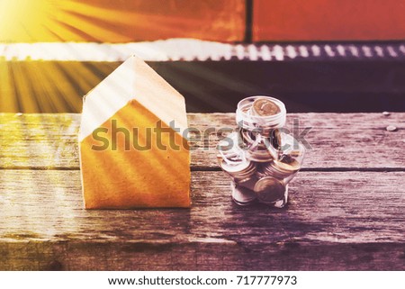 Stack of coins with miniature of small paper house isolated on wooden table background, dream light effect. House and money concept. Abstract conceptual image.