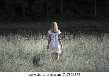 Back view of lonely sad blonde girl on the sunny meadow field. 