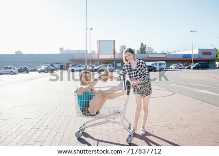 Girls drink alcohol at the supermarket. Young women with a supermarket car. Party at the parking lot near the store.