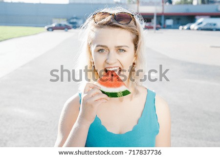 a girl with a juicy watermelon. Woman is looking for a fruit. A warm sunny day at the parking lot near the store.