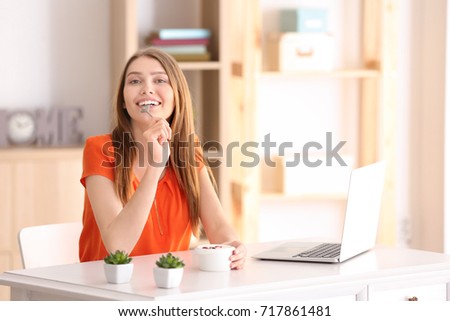 Young woman eating yogurt at table