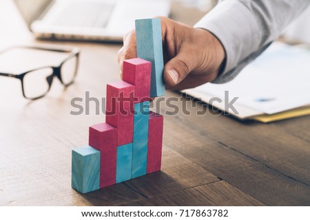 Businessman working at office desk, he is building a growing financial graph using wooden toy blocks: successful business concept Royalty-Free Stock Photo #717863782