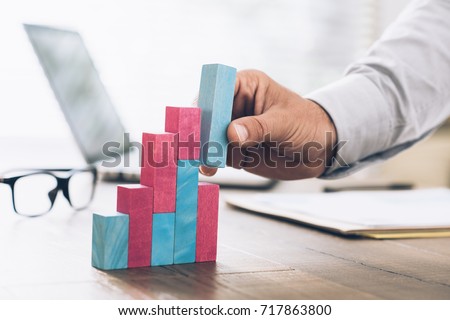 Businessman working at office desk, he is building a growing financial graph using wooden toy blocks: successful business concept Royalty-Free Stock Photo #717863800